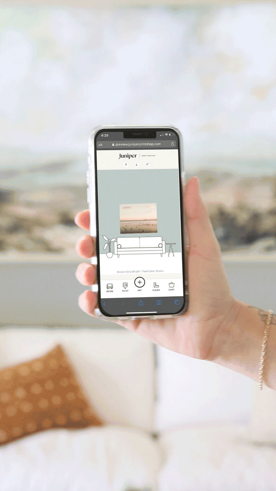 A hand holding a smart phone that is displaying Juniper's Print Preview - a tool that helps you visualize oversized art in your home.
