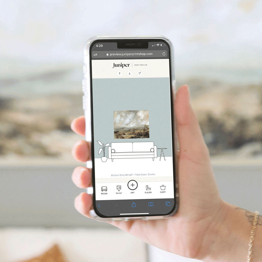 A hand holding a smart phone that is displaying Juniper's Print Preview - a tool that helps you visualize oversized art in your home. 
